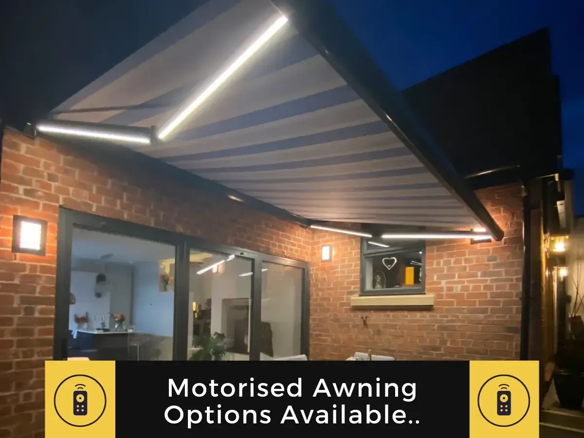 An illuminated striped retractable awning over a glass patio door on a brick wall at night, featuring motorized options.