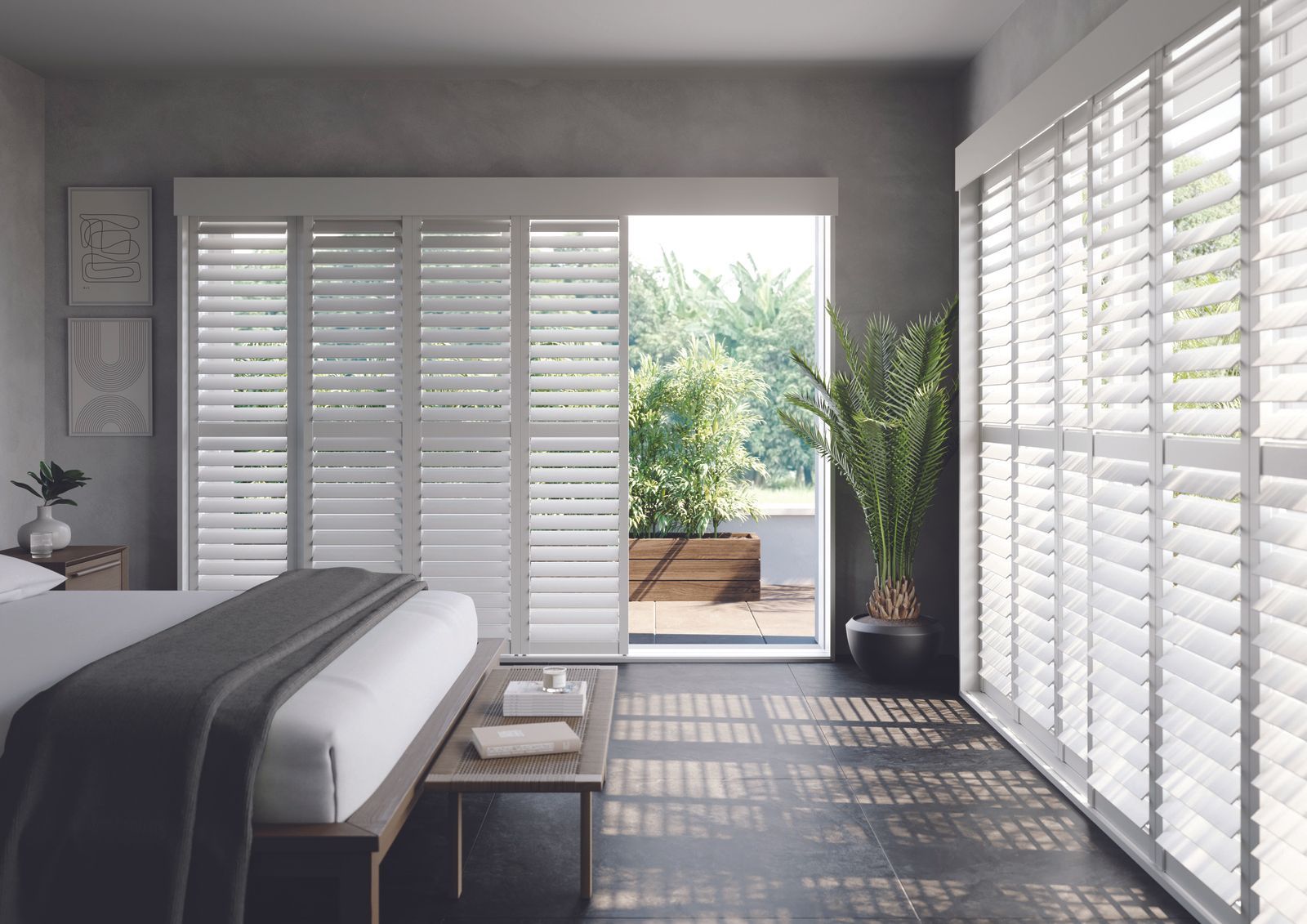 A modern bedroom with white sliding shutters, a bed with a grey throw, and a potted plant by a balcony door.