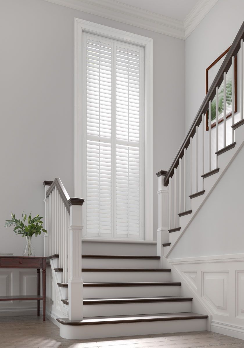 Staircase with dark wood treads and white risers, leading to a tall, shuttered window in a neutral-toned hallway.