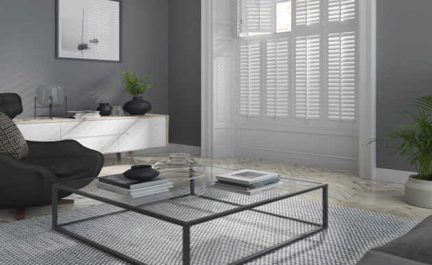 A modern living room with a black armchair, glass coffee table, white cabinet, and gray walls with window shutters.