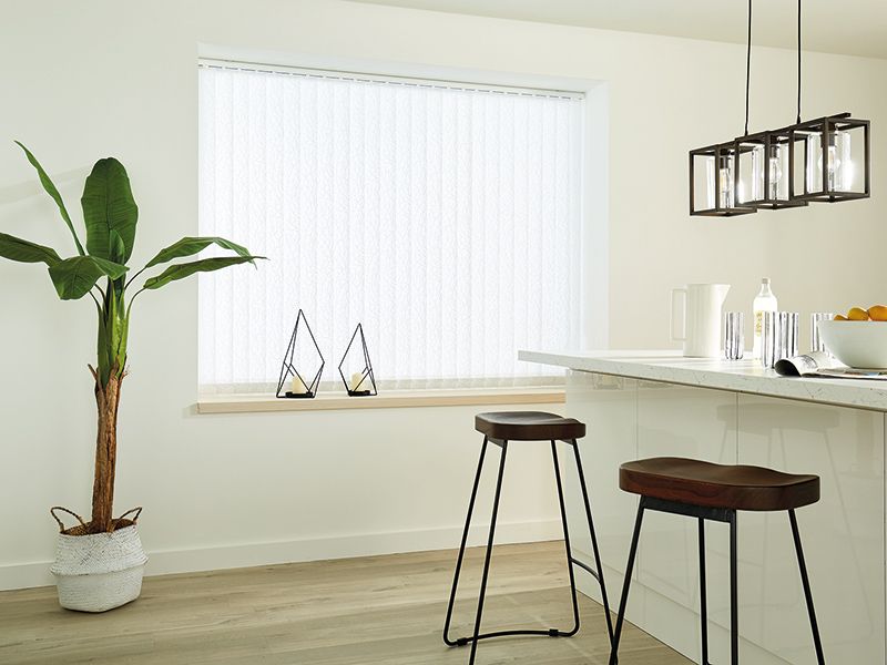 A kitchen island with two wooden bar stools, a tall potted plant, and a large window with white vertical blinds.