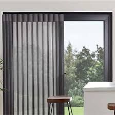 A floor-to-ceiling vertical blind covering a sliding glass door with a view of trees outside.