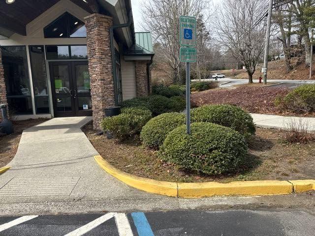 Accessible parking space beside building entrance with curb, sidewalk, and shrubs