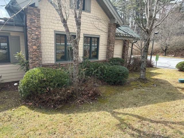 Brick house corner with windows, shrubs, and a grassy yard on a sunny day