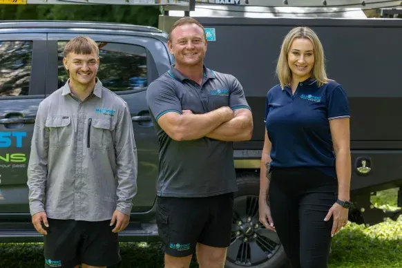 Three people stand in front of a truck. Two men and a woman in work attire smile.