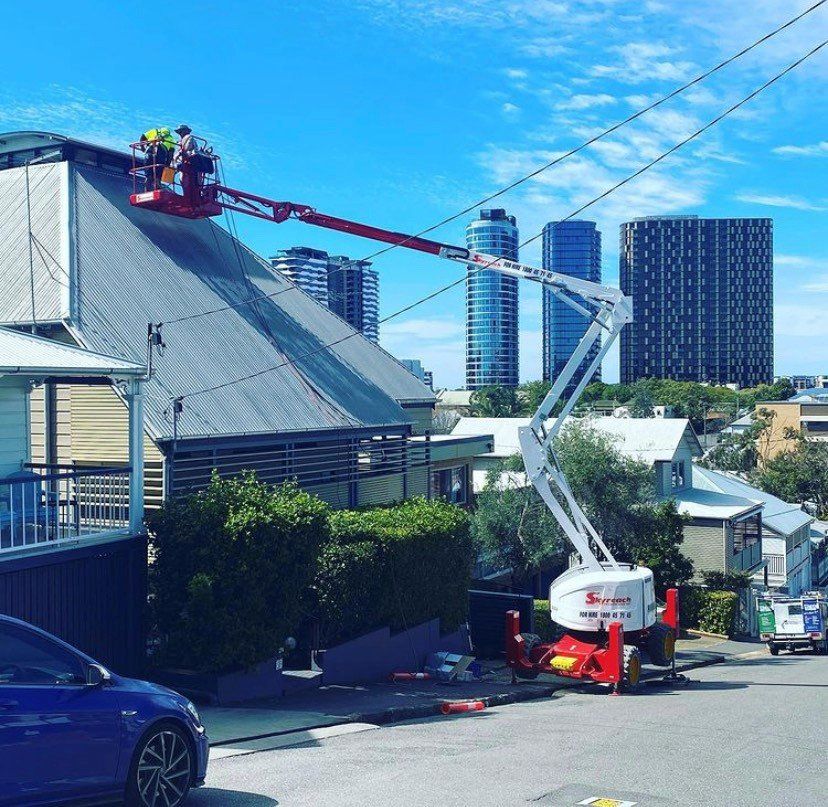 Workers on an extended boom lift repairing a roof, with city skyline in the background.