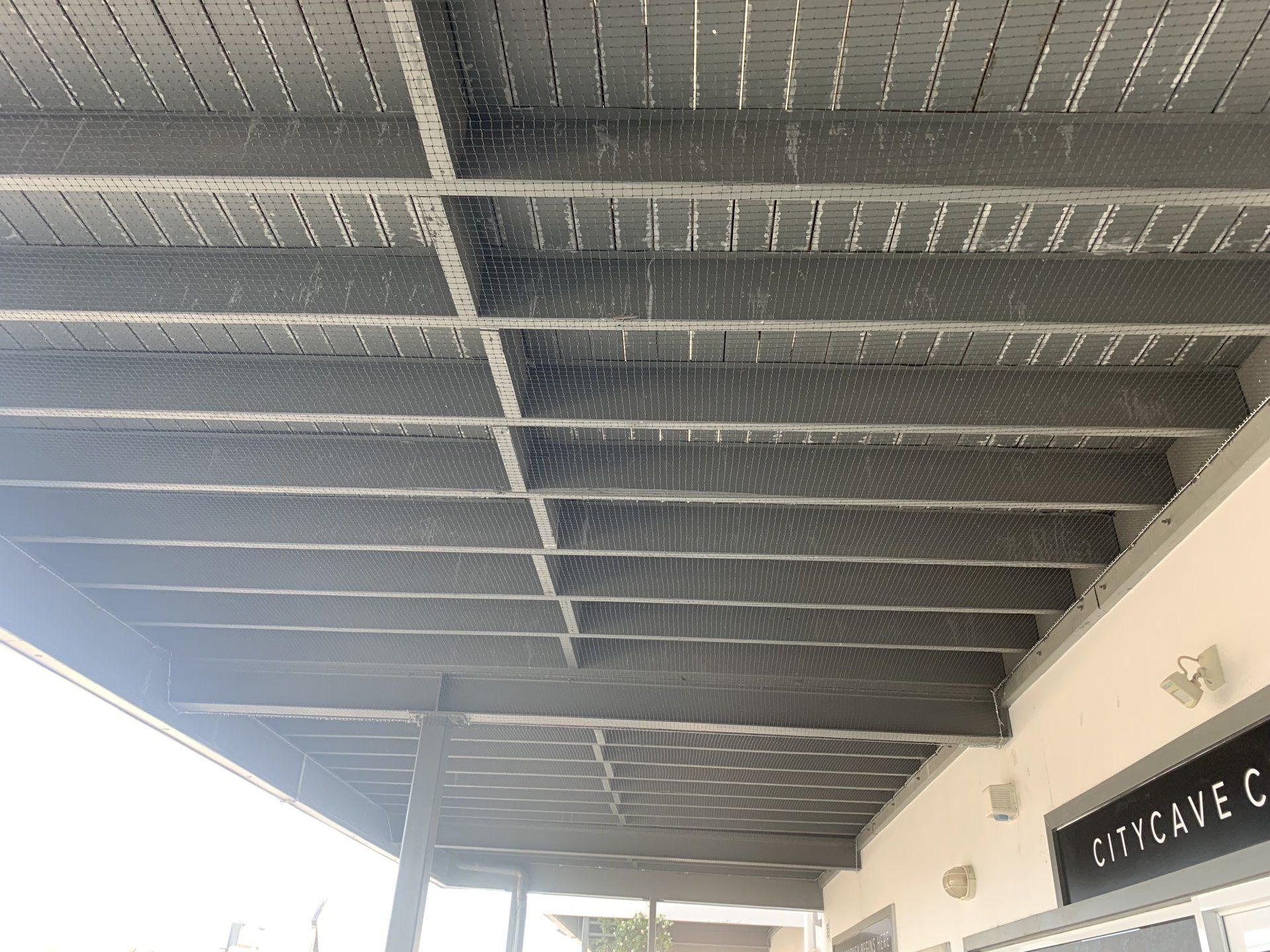 Gray painted slatted ceiling with mesh; part of a building facade.