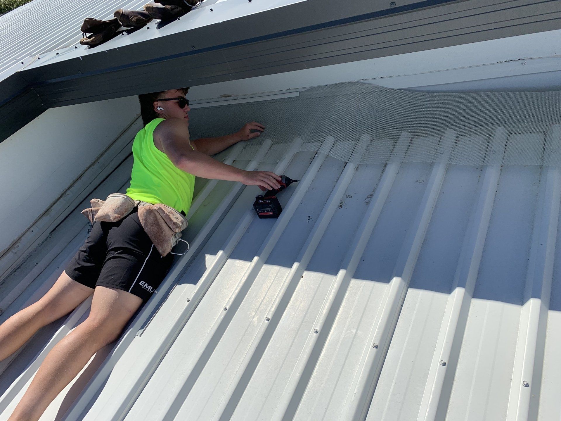Person in neon green shirt on a metal roof, using a drill.