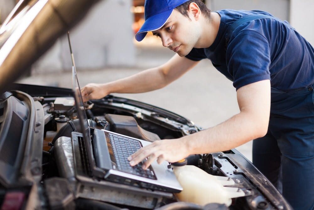 A Man is Working on a Car With a Laptop — Clarence Valley Auto Electrical in South Grafton, NSW