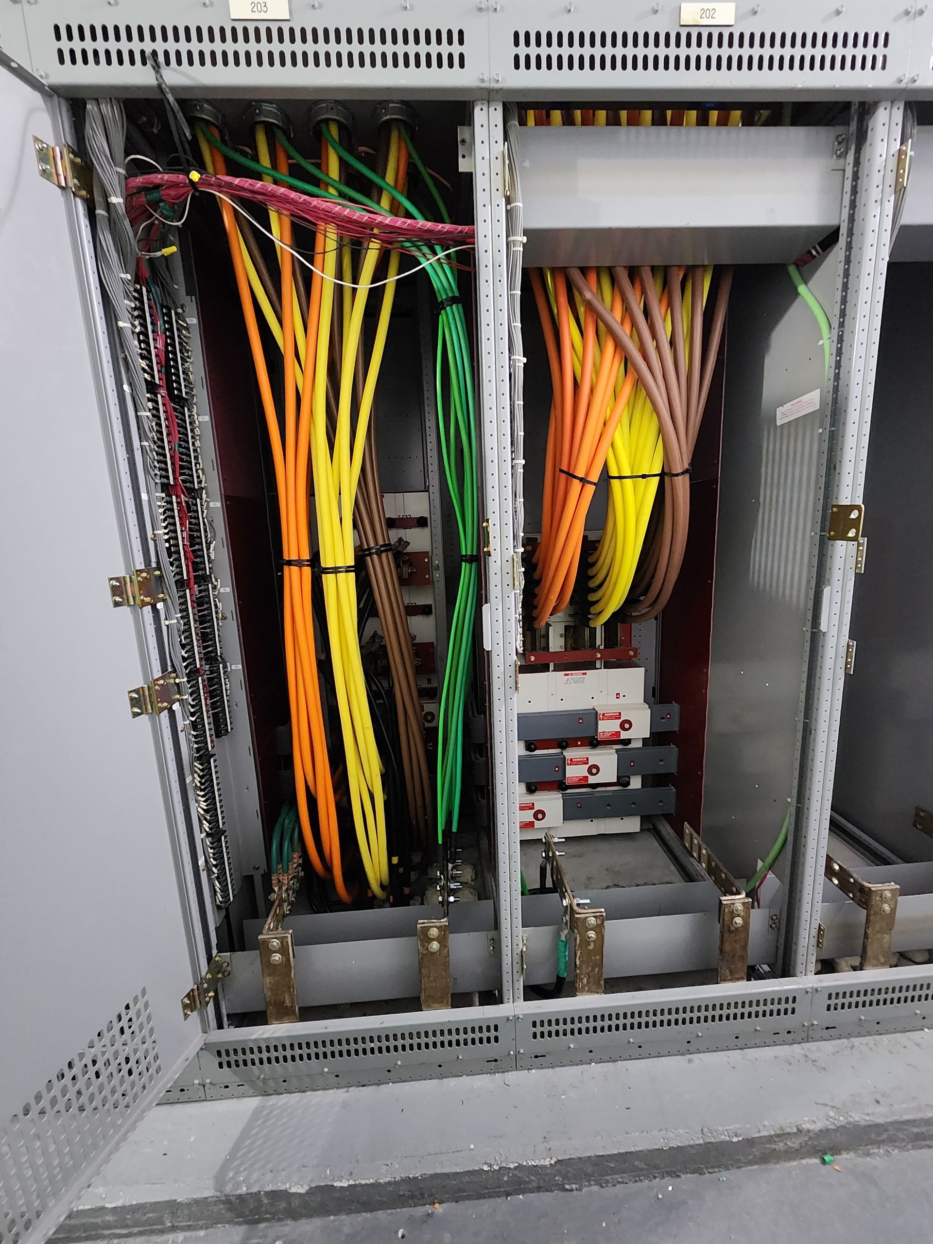 Open electrical cabinet with bundles of yellow, green, and orange cables inside
