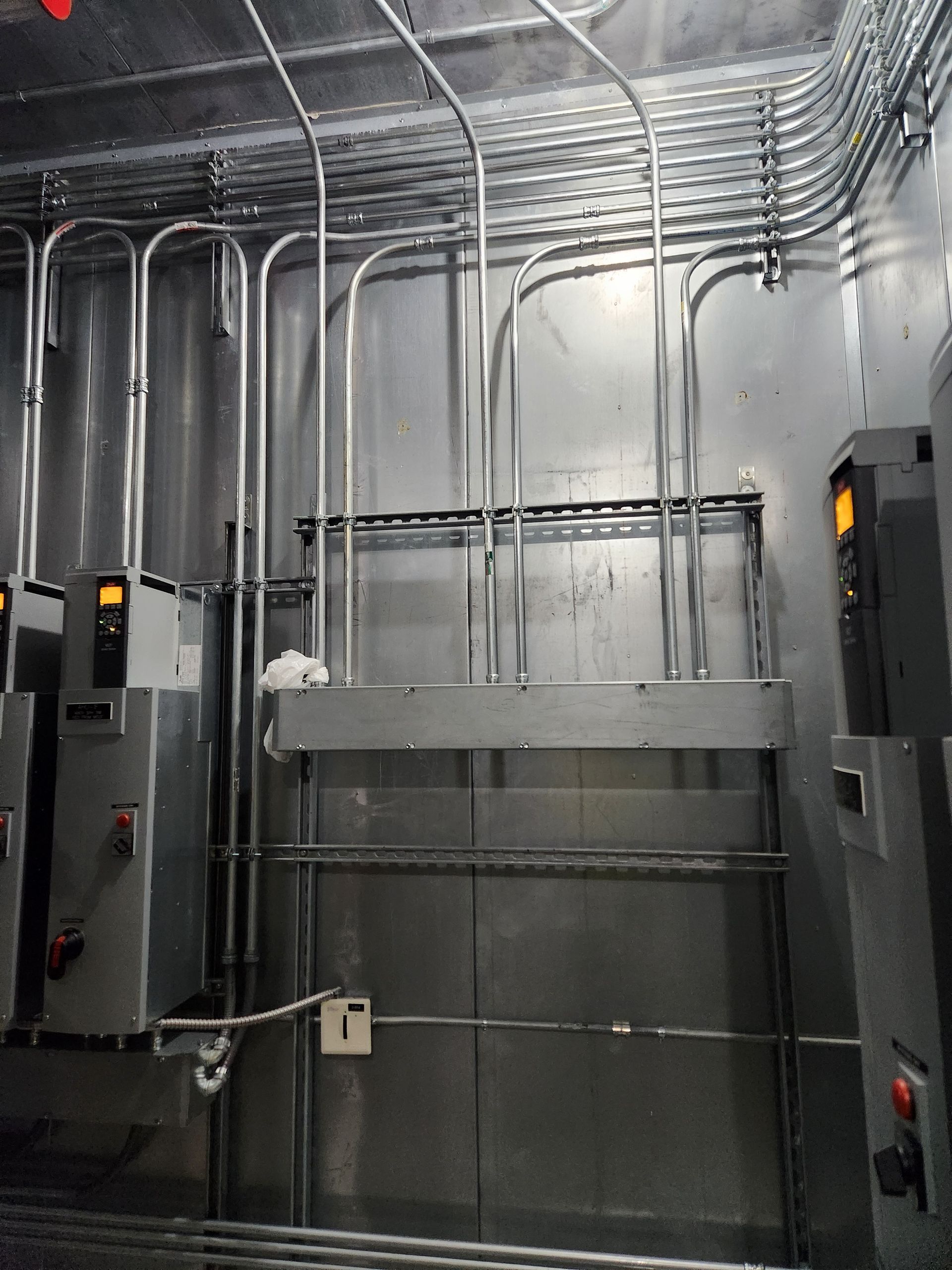 Metal elevator shaft with exposed wiring and gray panels, viewed from inside an industrial room