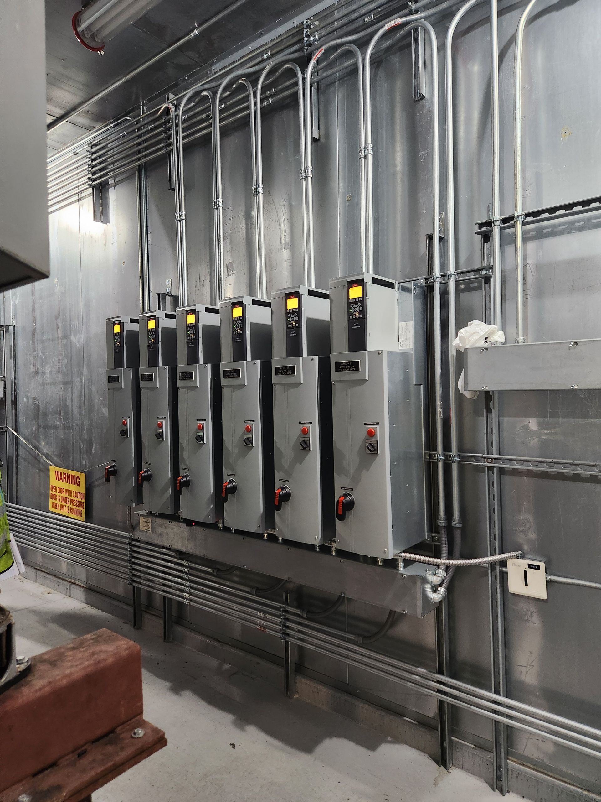 Electrical control panel with gray breaker boxes and conduit on a warehouse wall