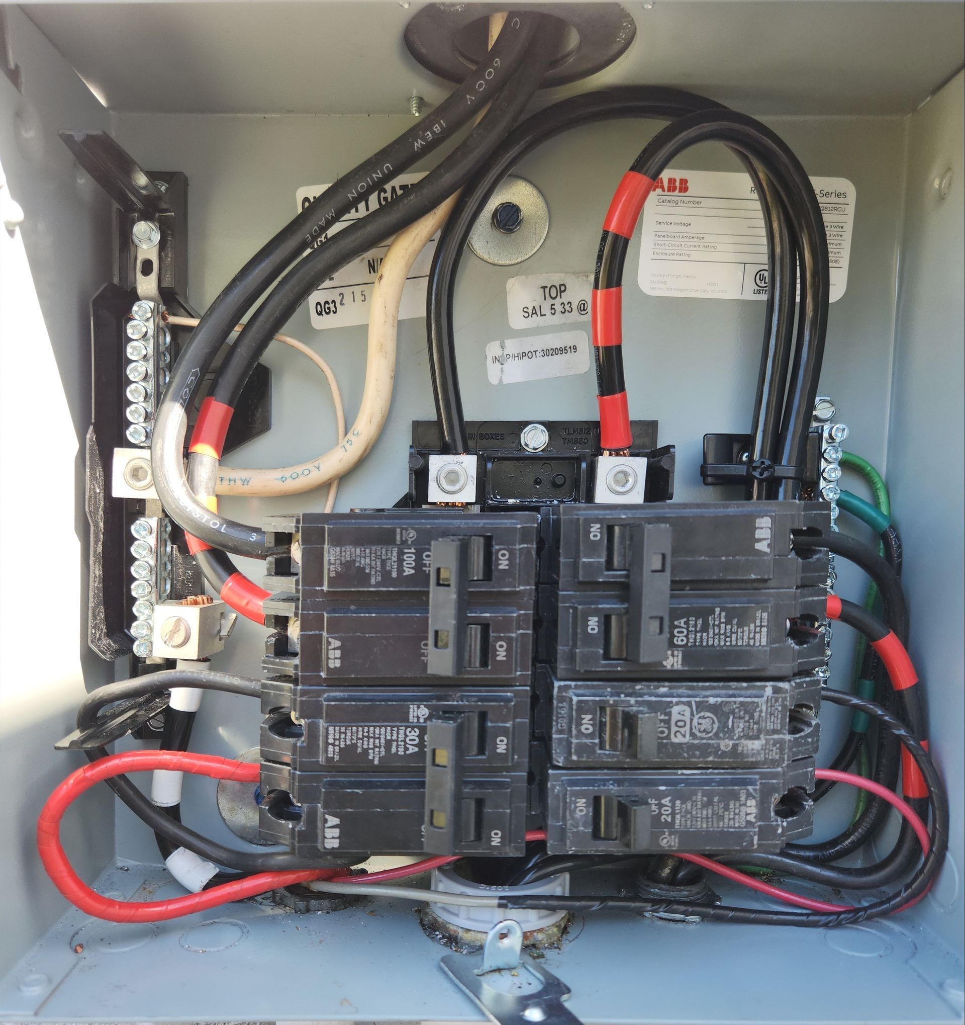 Open electrical breaker panel with black breakers, red and black wires, and meter inside a gray cabinet