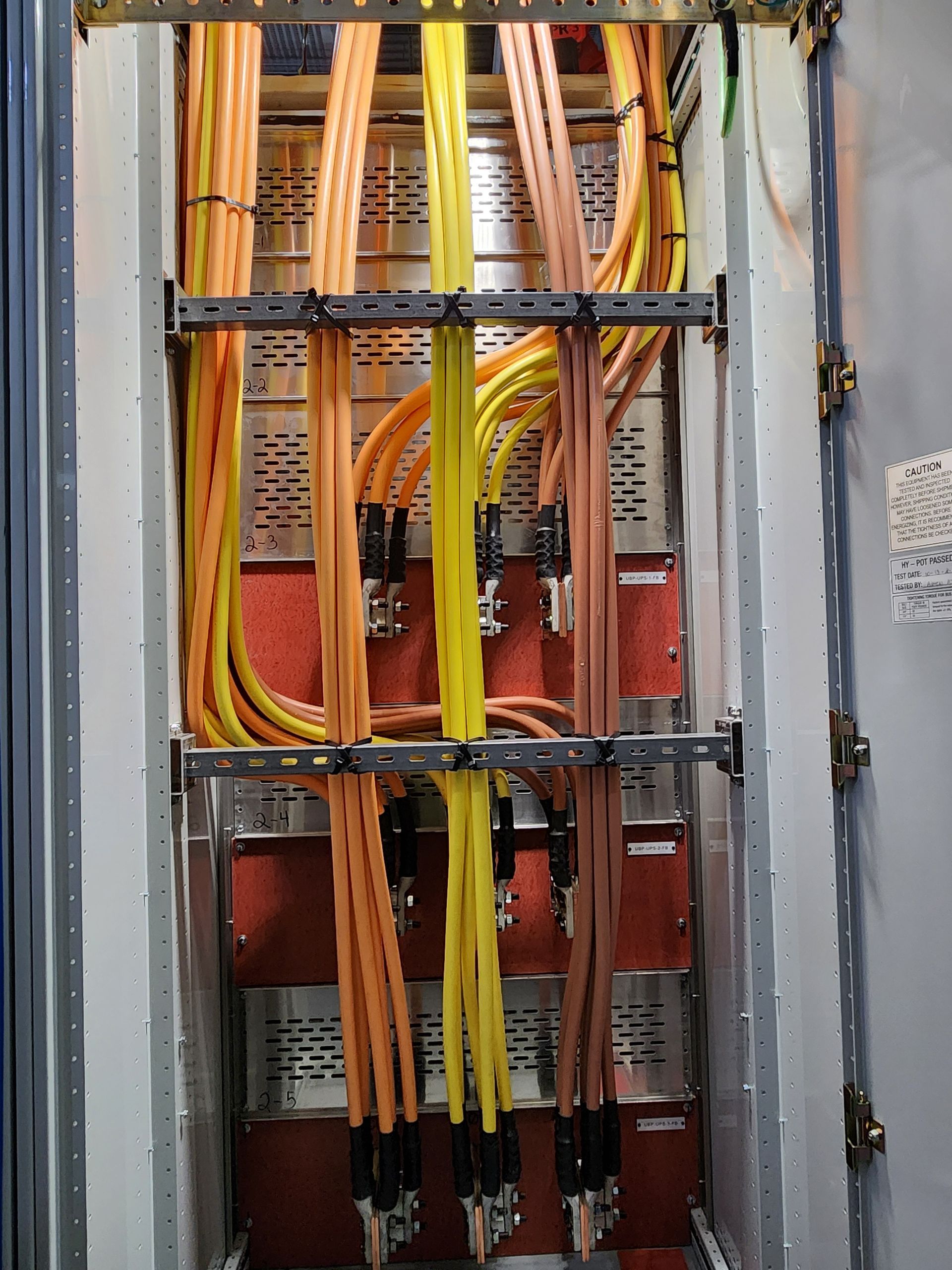 Network cables bundled in a wall rack, with orange and yellow wires running vertically through metal brackets