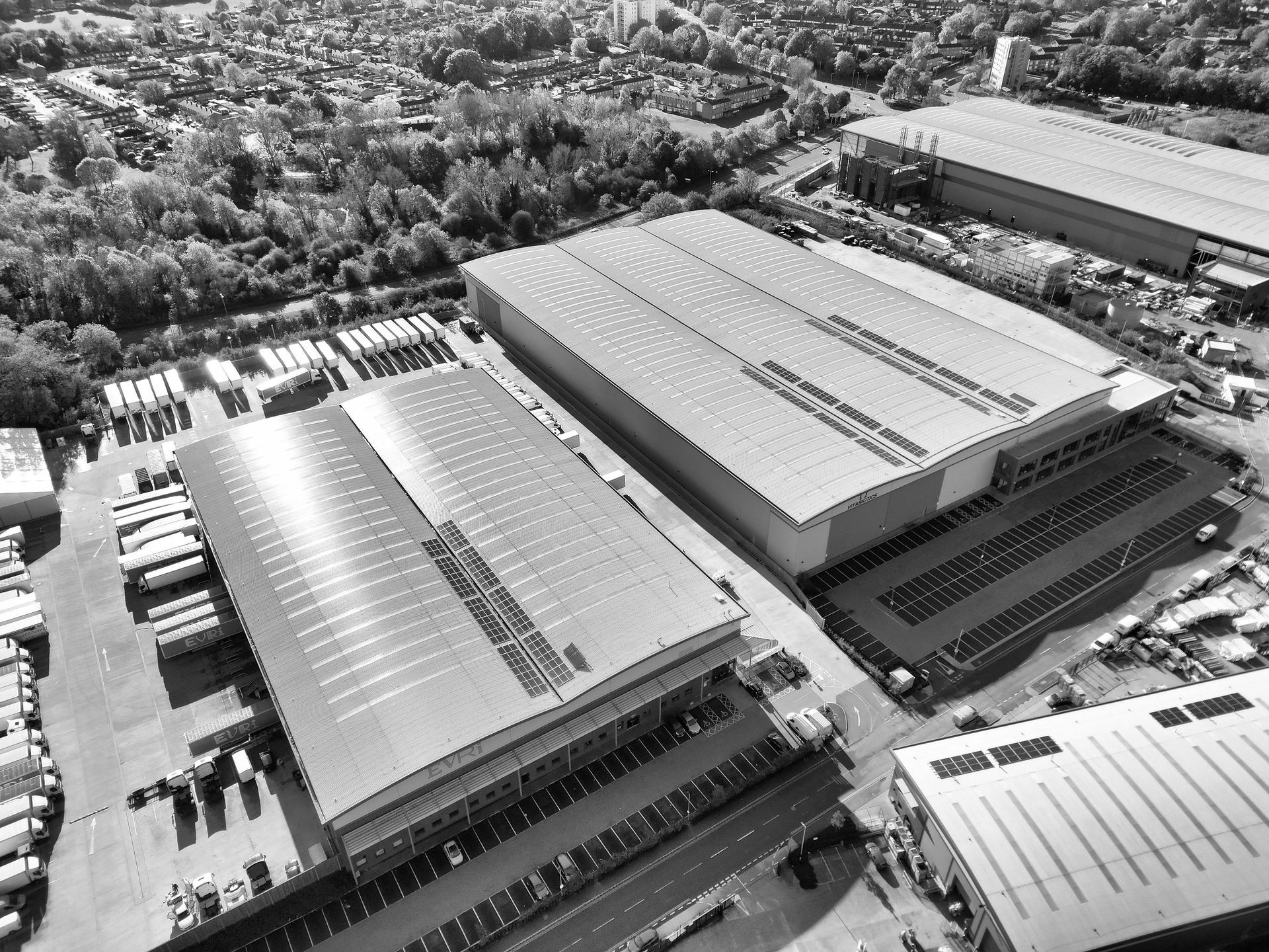 Aerial view of large industrial warehouses and parked trucks in a tree-lined business park