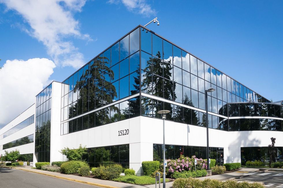 Modern glass office building with mirrored windows and white exterior, viewed from the street
