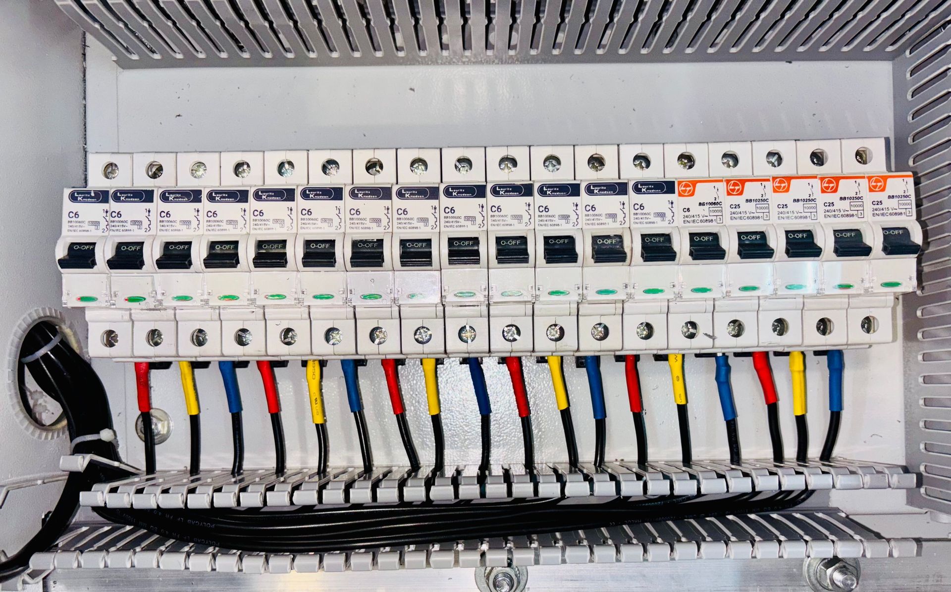 Electrical breaker panel with rows of circuit breakers and colored wires connected below