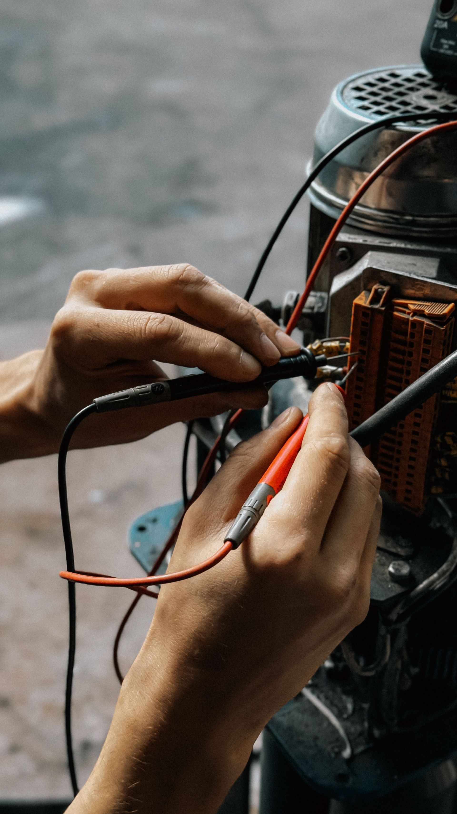 Hands connecting red and black wires to an electrical device with exposed components.