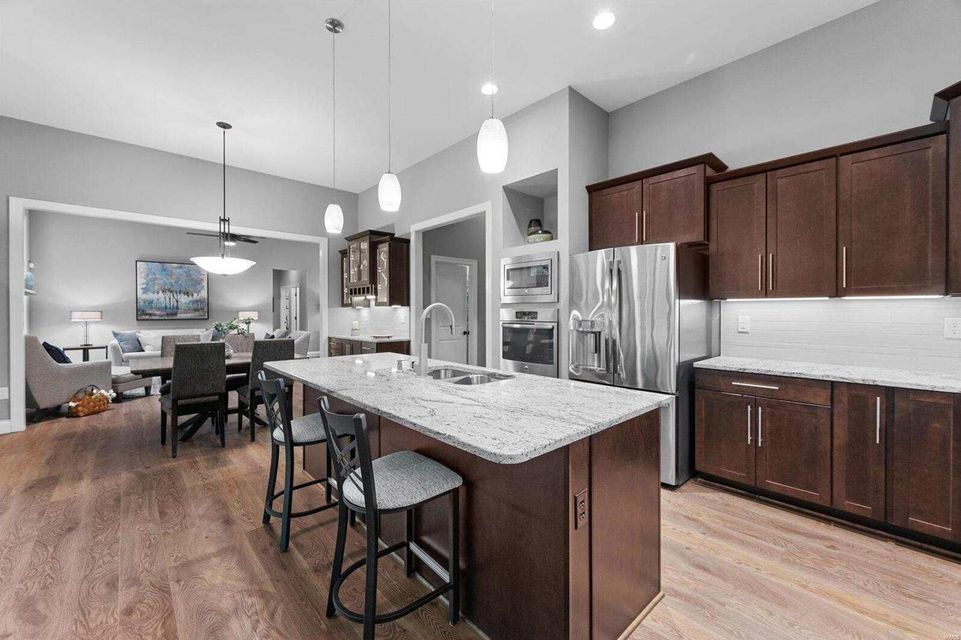 Modern kitchen with dark wood cabinets, a granite-topped island with two stools, and a view into a dining area.