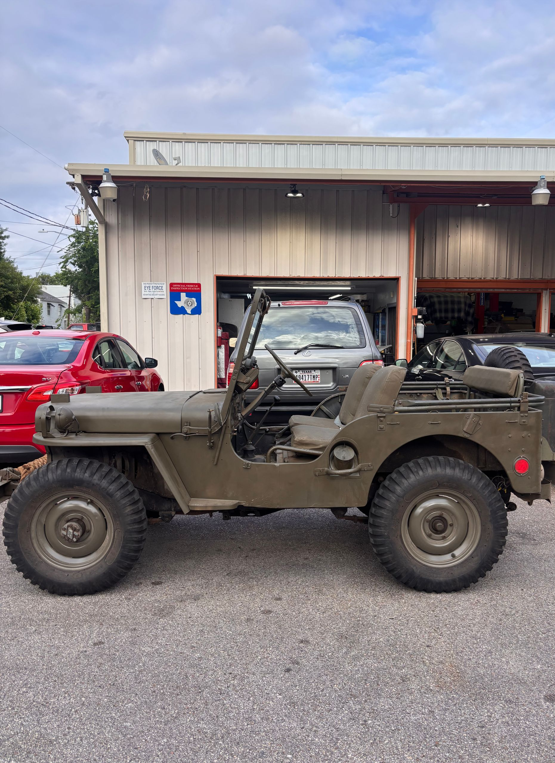 Olive drab vintage military jeep parked on gravel outside a metal garage.