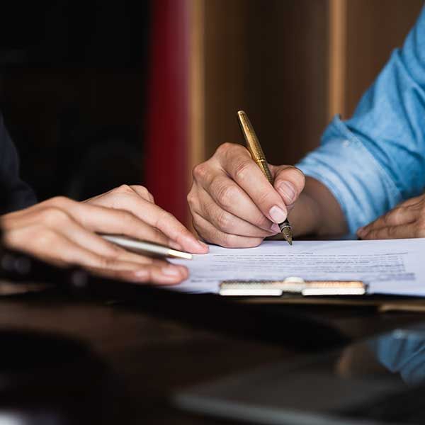 Hands signing a document at a desk, with a clipboard in the foreground