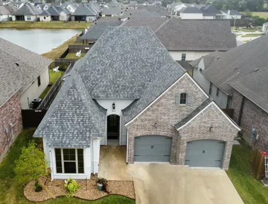 Aerial view of a gray-shingled suburban house with a two-car garage and driveway.