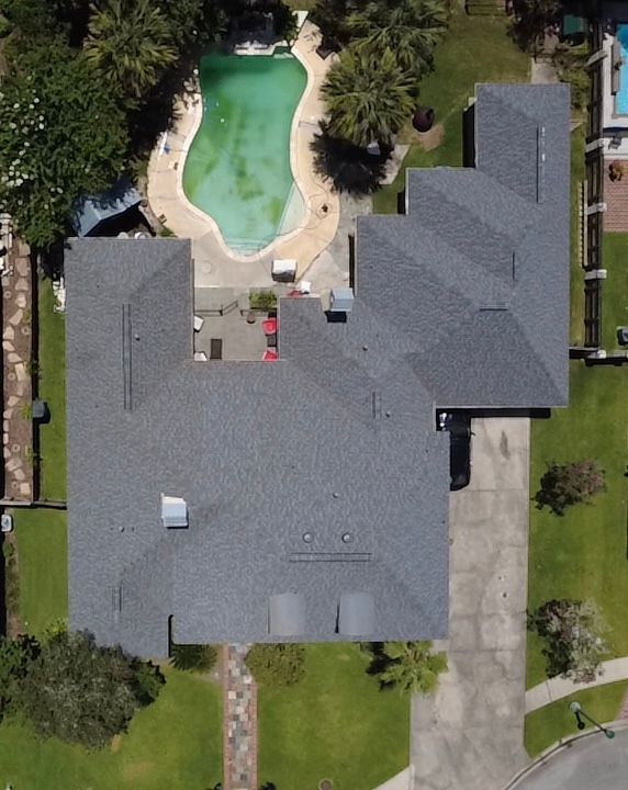 Aerial view of a house with a gray roof, driveway, lawn, and backyard pool.