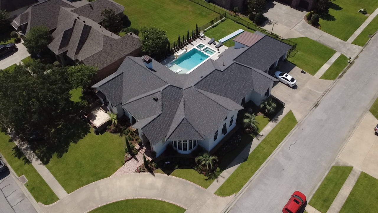 Aerial view of a suburban house with a backyard pool, lawn, driveway, and nearby street.