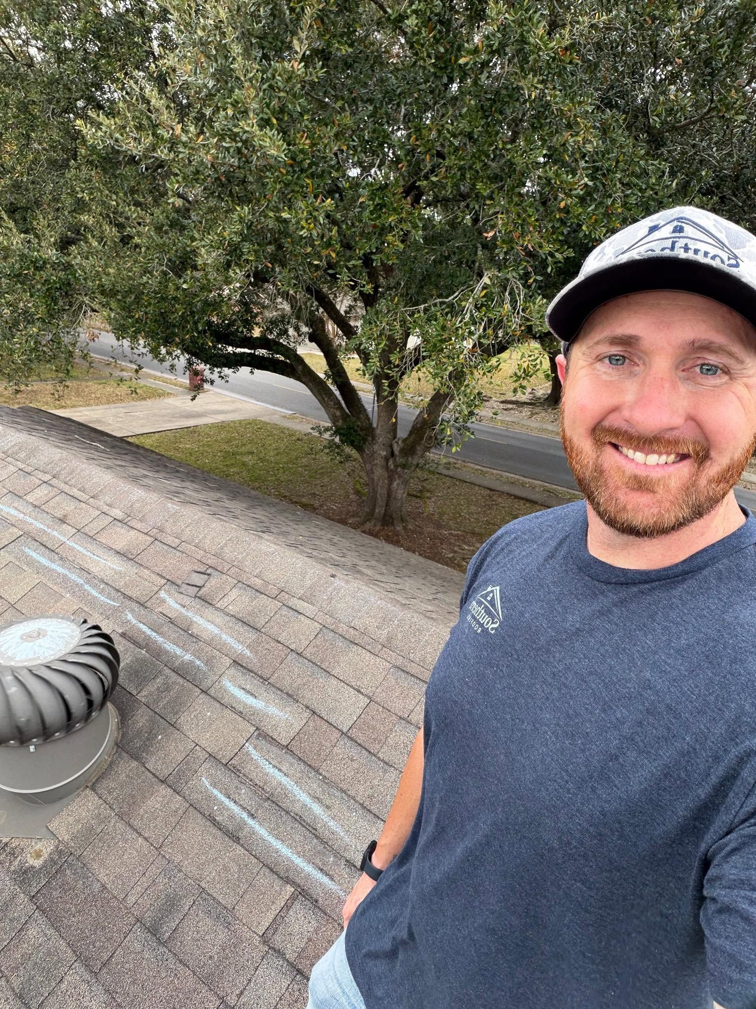 Smiling person in a cap taking a rooftop selfie near a tree and a street below