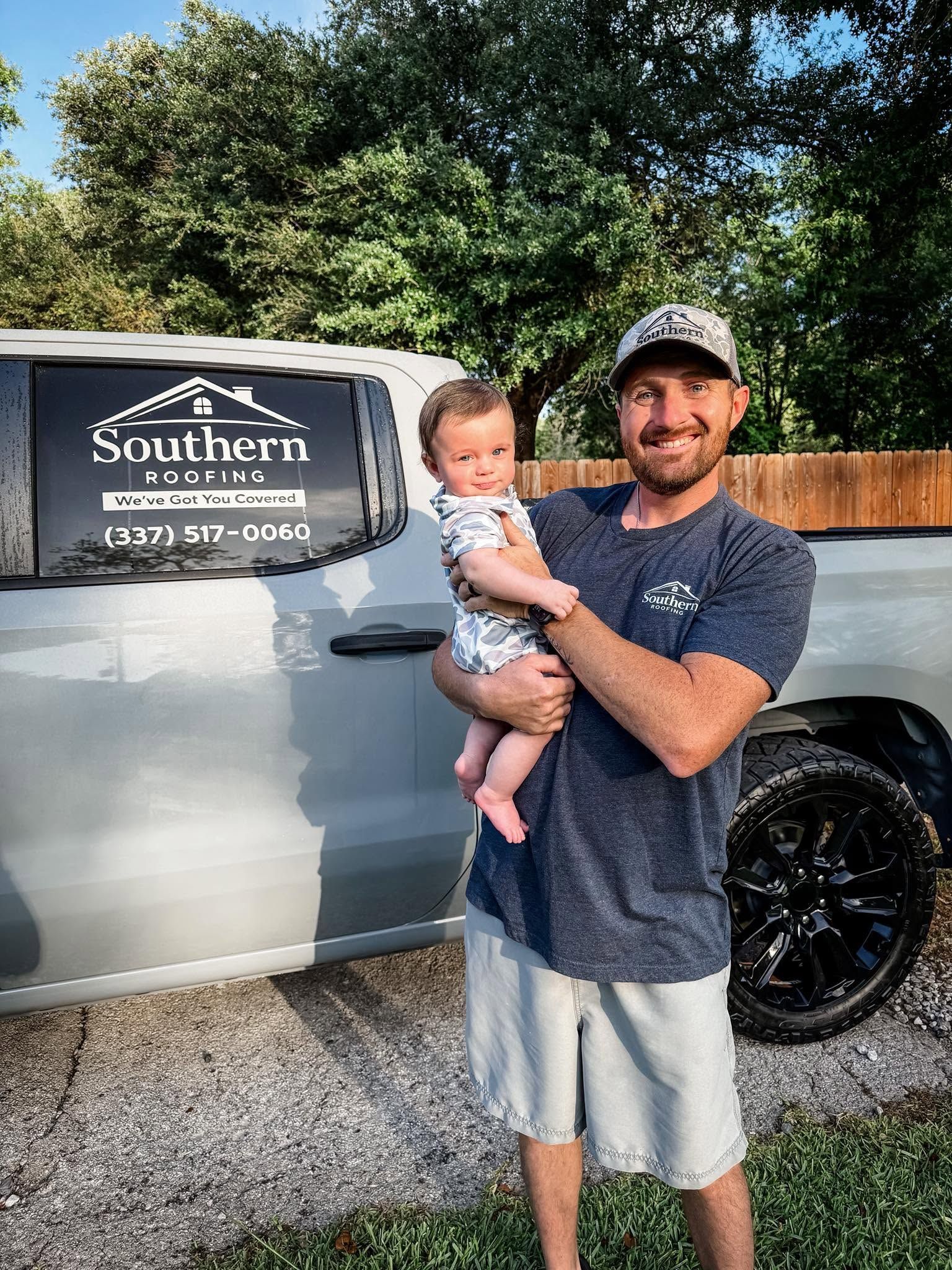 Man holding a baby beside a silver truck with a Southern sign on the door.