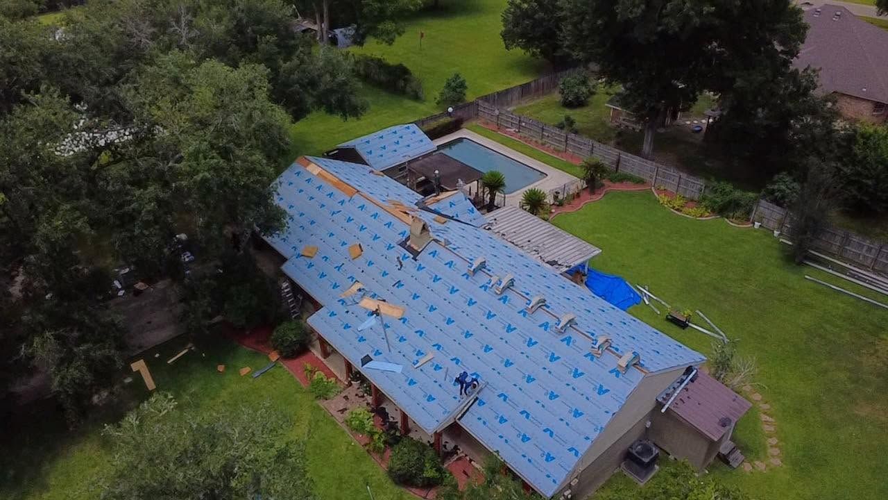 Aerial view of a large blue-roofed building surrounded by trees and greenery.