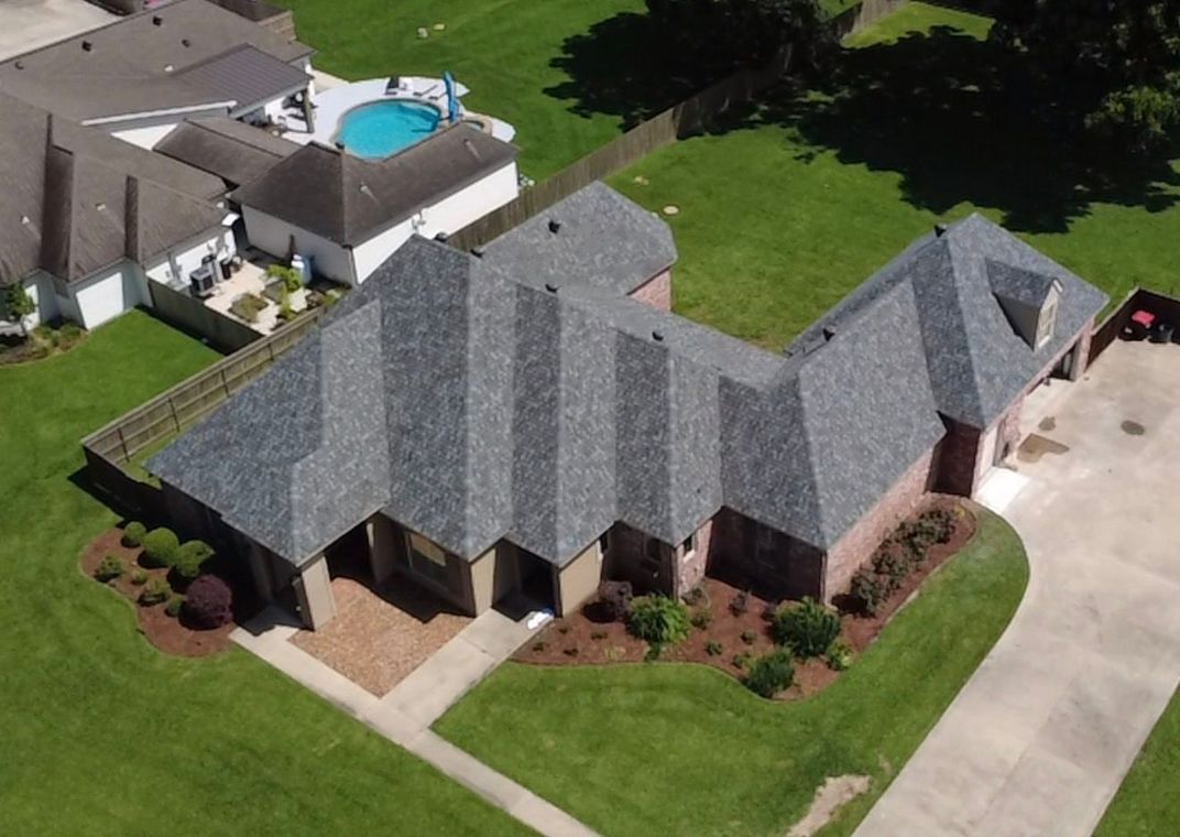 Aerial view of a gray-roofed suburban house with a driveway, lawn, and backyard pool
