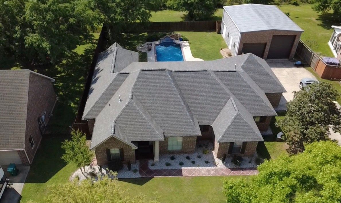 Aerial view of a gray-roofed suburban house with a backyard pool and detached garage.
