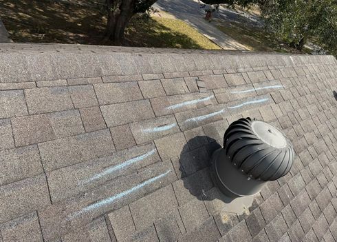 Black roof vent on a shingled rooftop with chalk lines marking a repair area