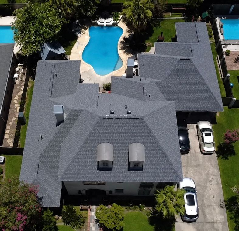Aerial view of a gray-roofed house with a backyard pool and two white cars in the driveway.