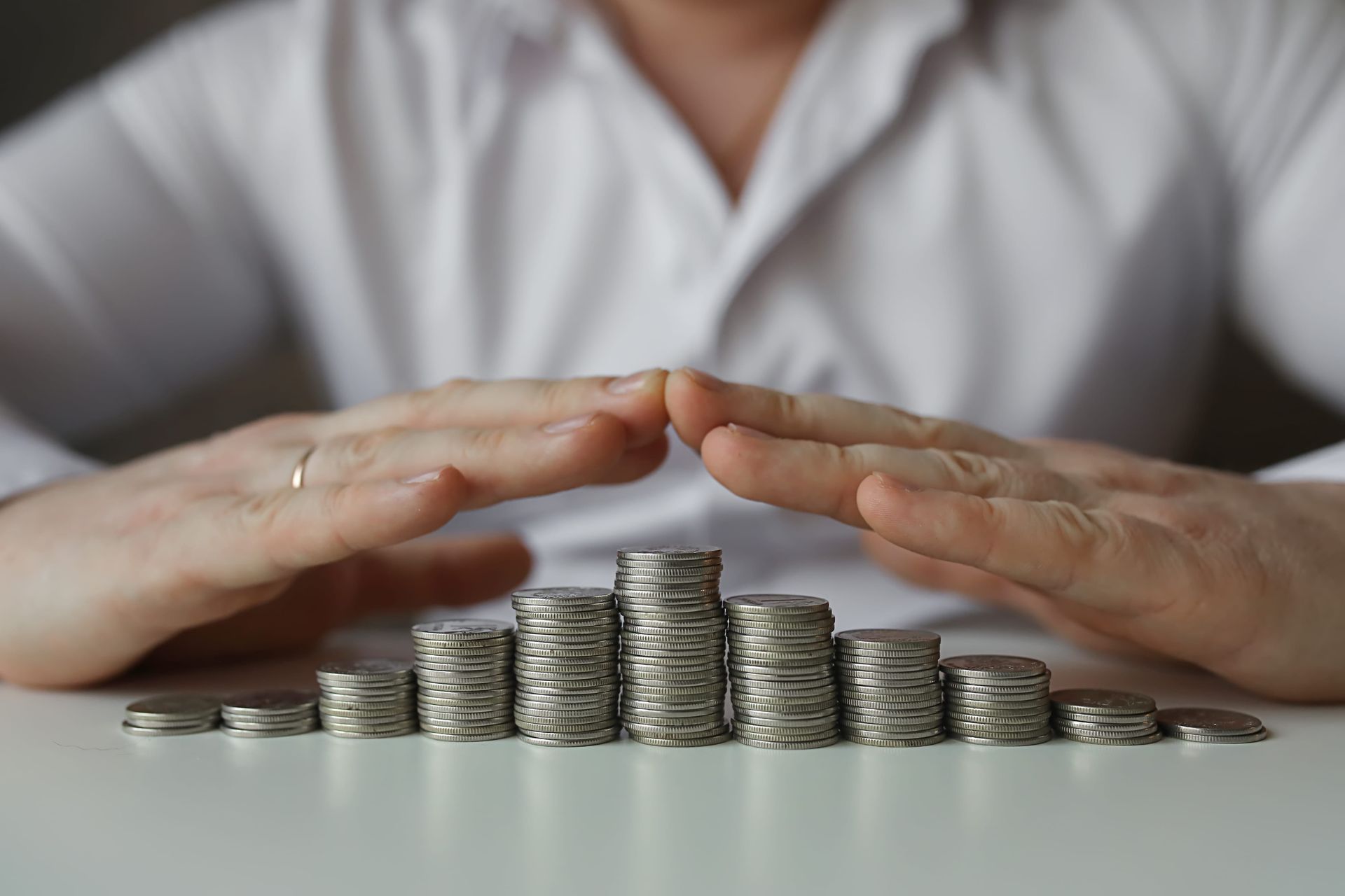Hands sheltering stacked coins on a table, suggesting savings or financial protection.