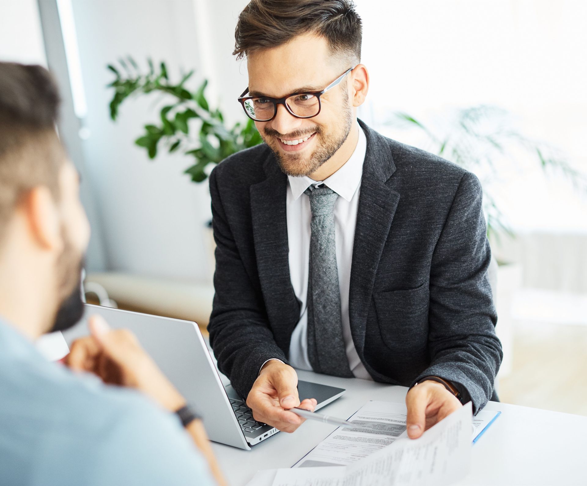Smiling man in a suit discussing documents across a desk in a bright office