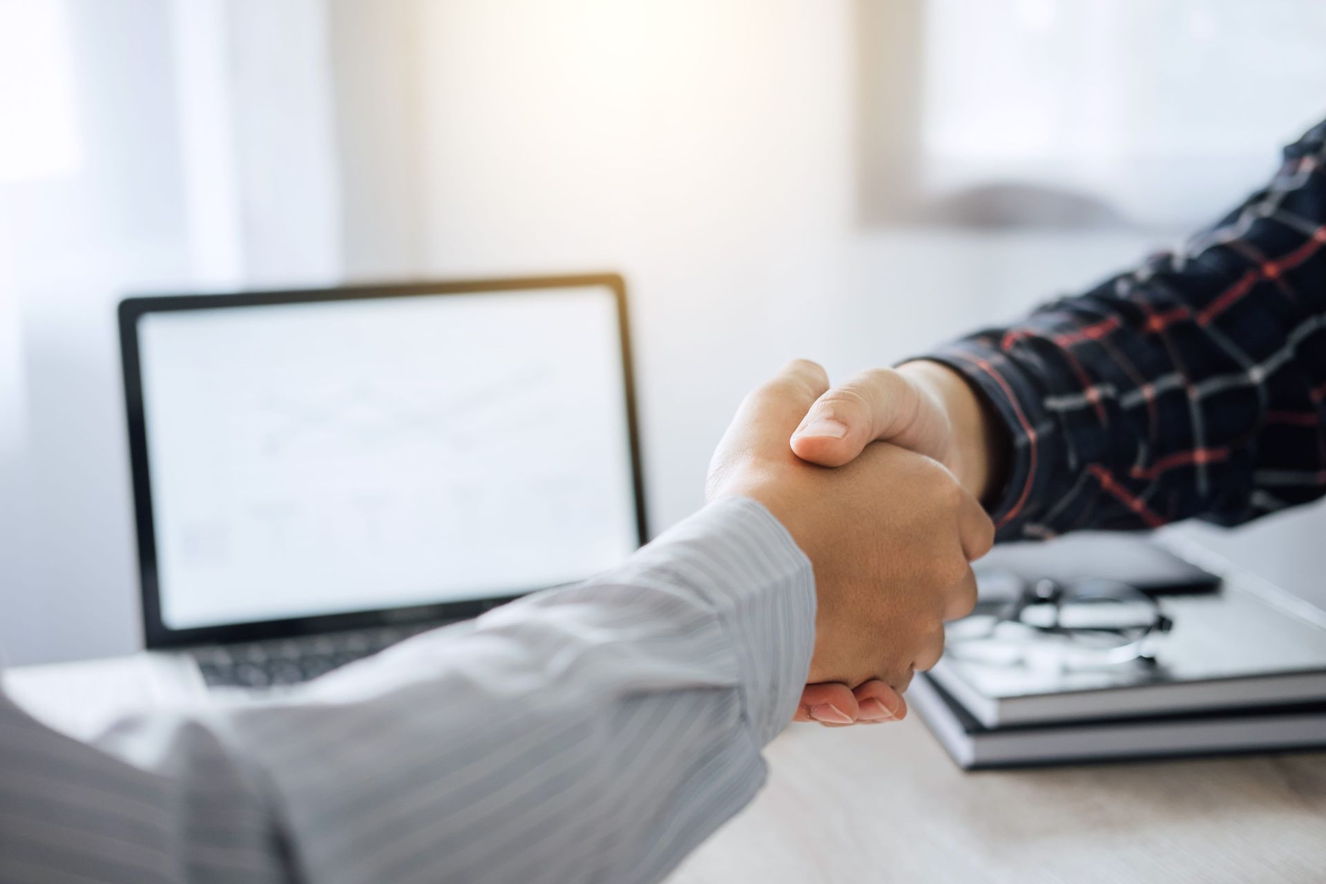 Handshake across a desk in an office, with a laptop in the background.