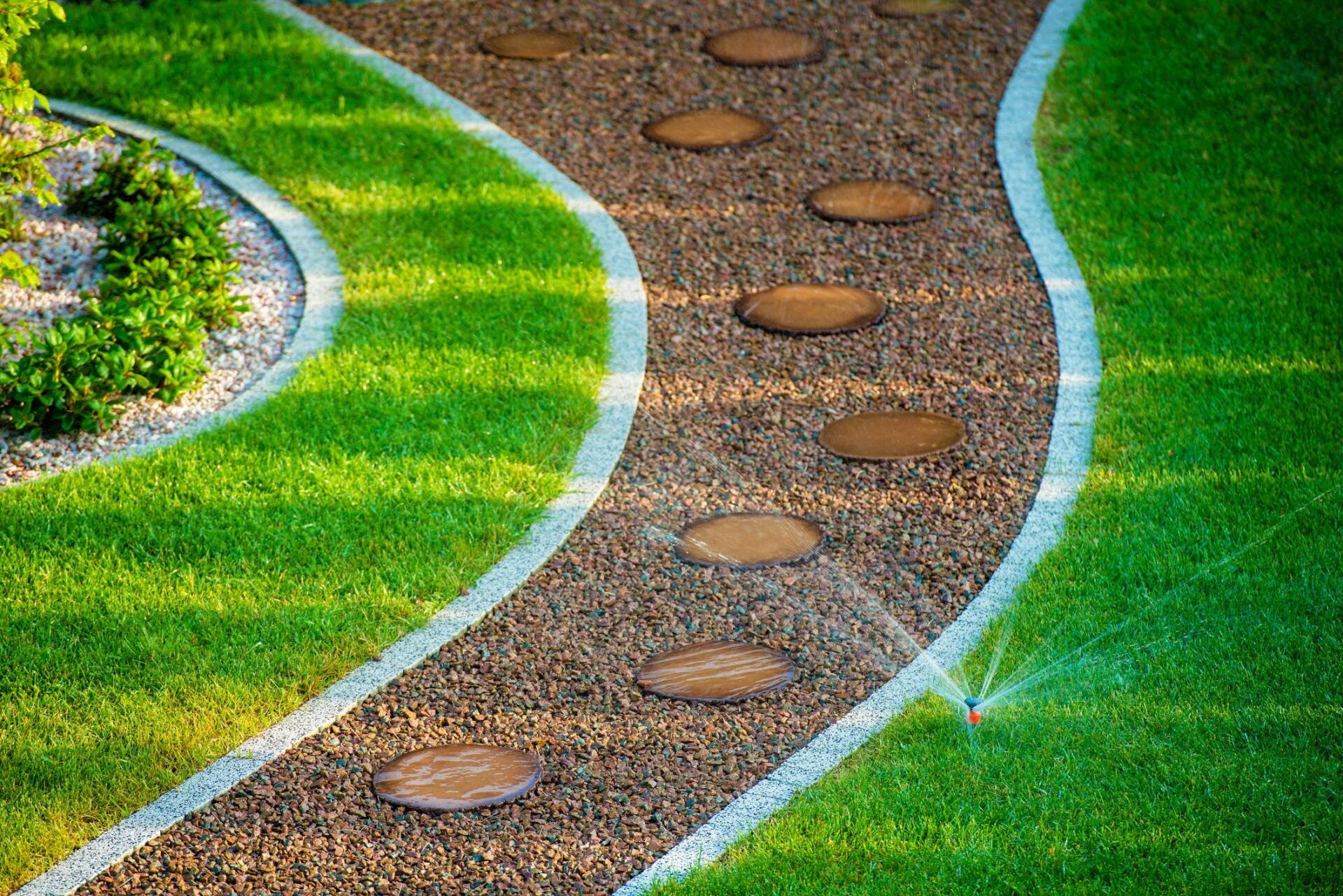 Irrigation systems at work in Residential Garden in Yorba Linda California. Gravel path with paved stepping stones surrounded by well kept grass being watered by a sprinkler head