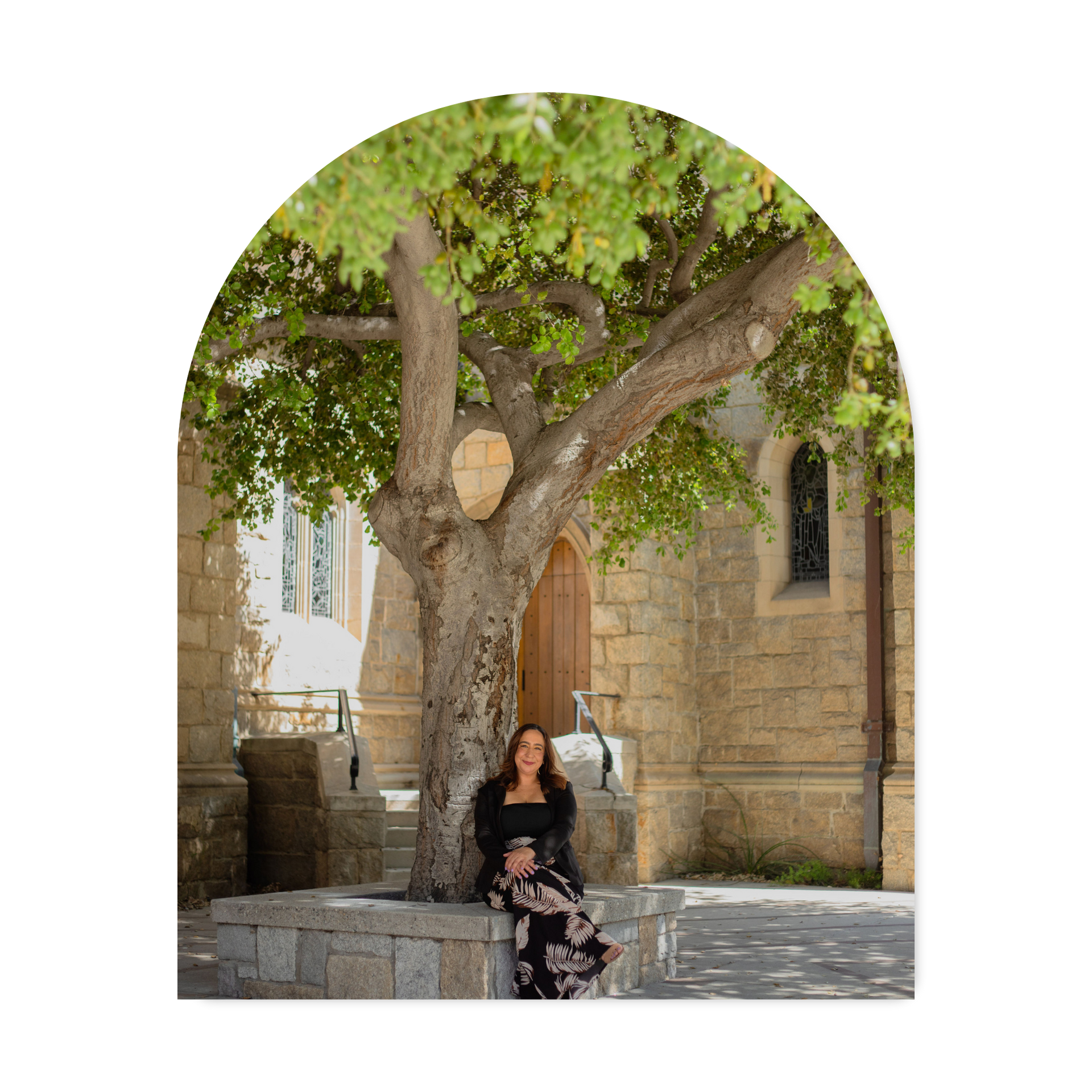 Woman seated beneath a large tree in a stone courtyard with a historic building in the background