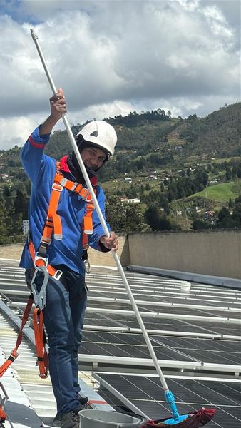 Un trabajador repara un tejado de tejas junto a una chimenea de ladrillo bajo un cielo nublado.