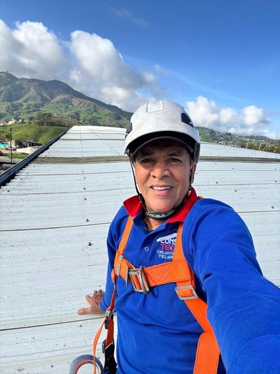Un trabajador con casco repara el tejado de una casa bajo un cielo azul despejado.