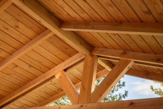 Vigas y tablones de madera forman un techo inclinado, dejando ver el cielo a través de la estructura.