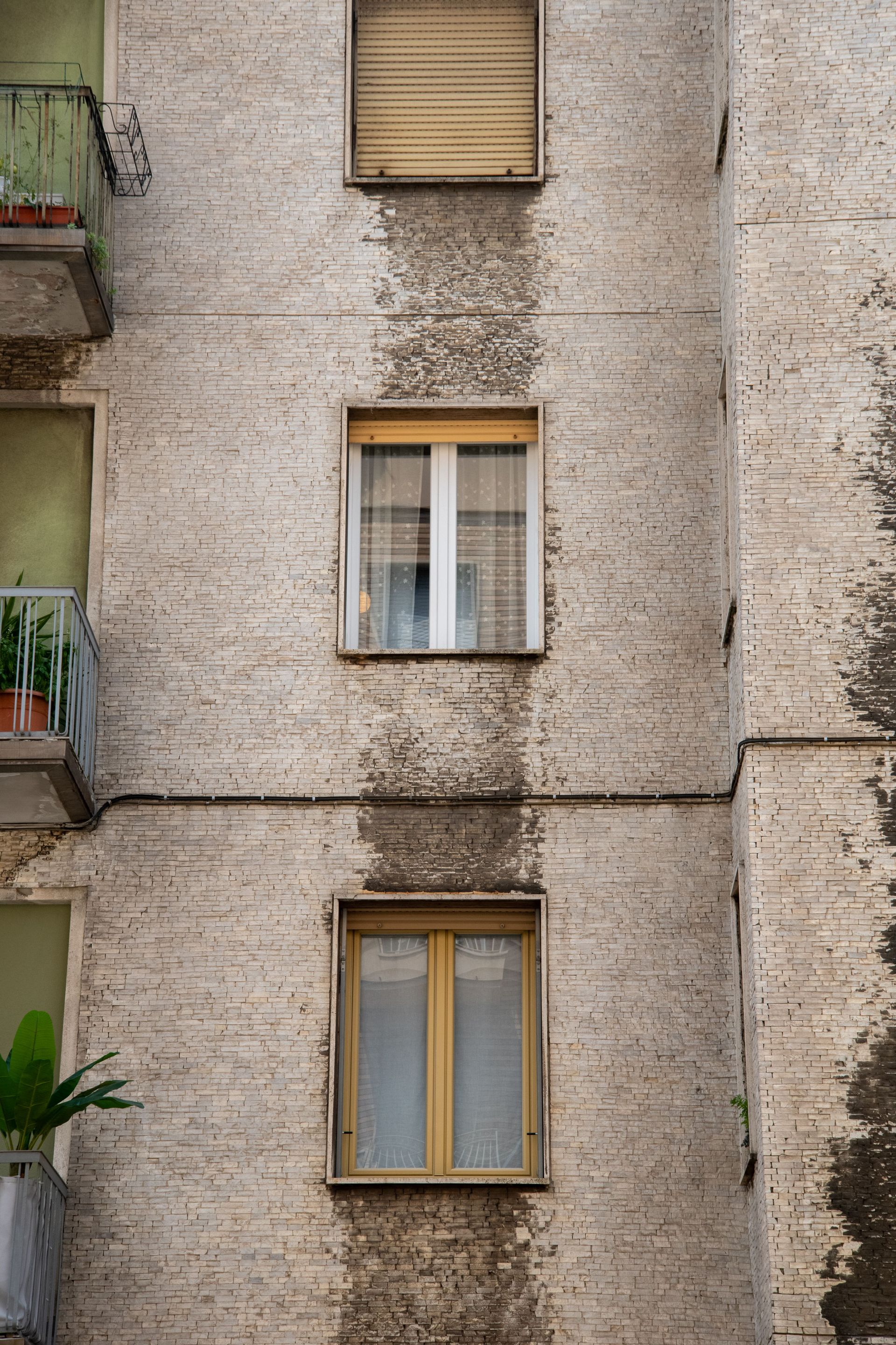 Fachada de un apartamento de ladrillo desgastado con tres ventanas y pequeños balcones a la izquierda.