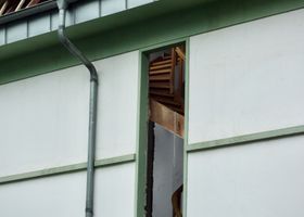 Panel de pared dañado con una grieta vertical debajo del borde de un techo verde.