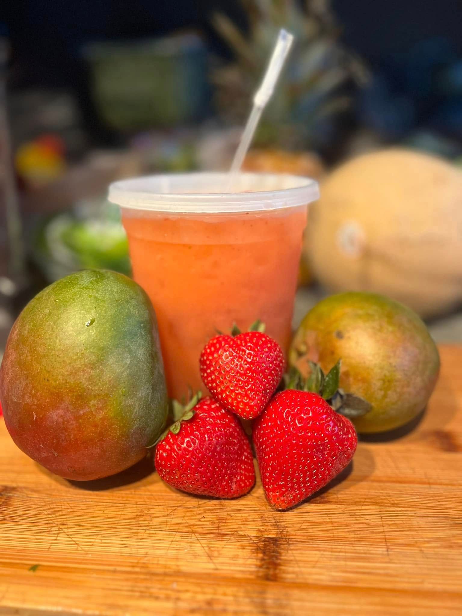 Mangoes, strawberries, and a cup of orange smoothie on a wooden table