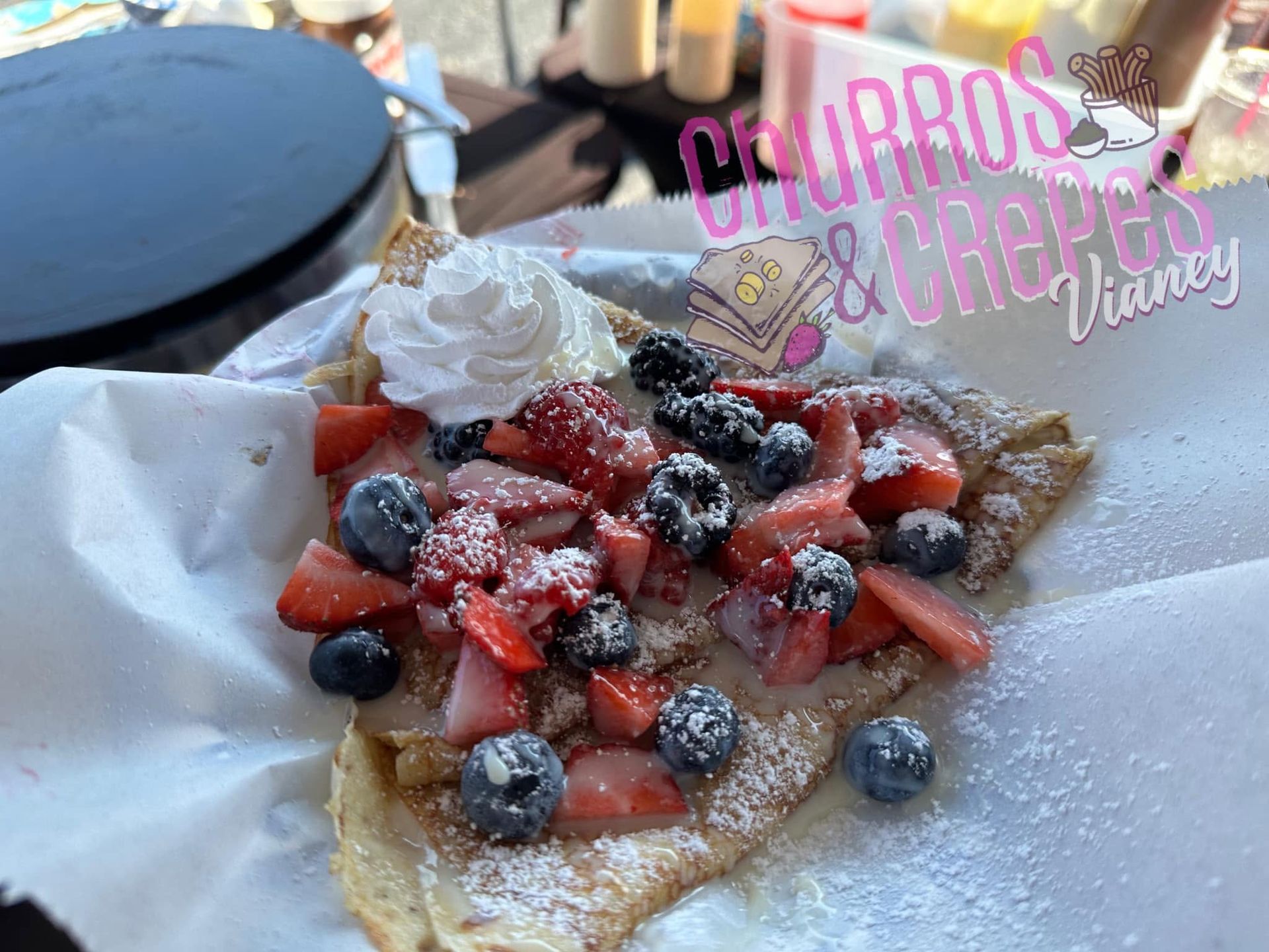 Crepe topped with strawberries, blueberries, whipped cream, and powdered sugar on a table