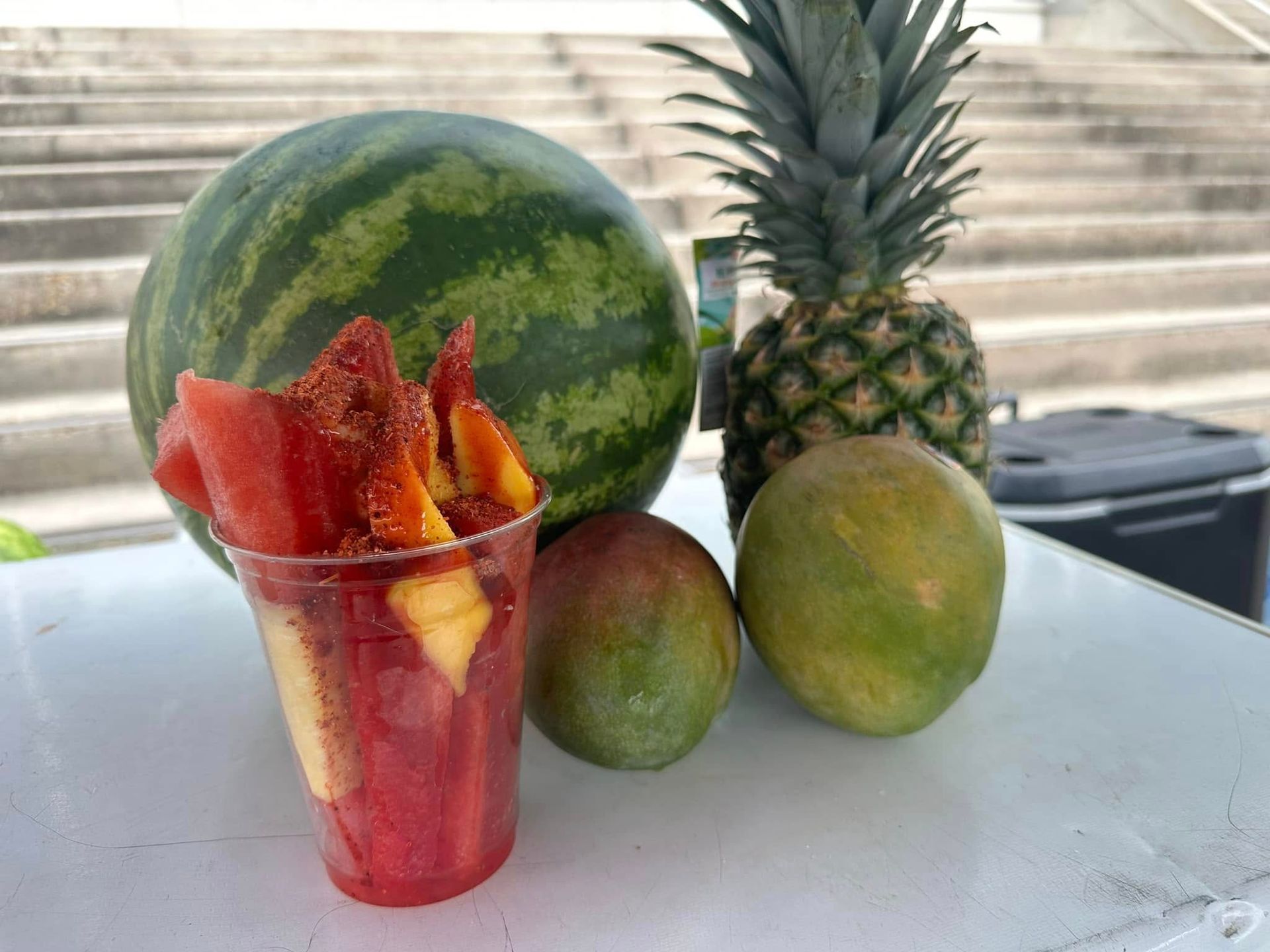 Cup of red fruit chunks with watermelon, pineapple, and mangoes on a white table