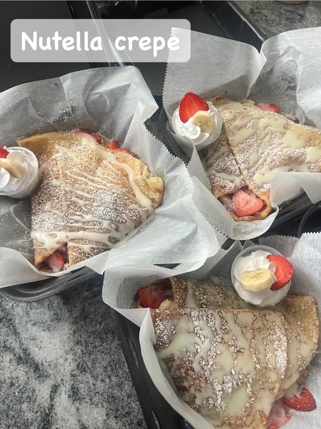 Nutella crepes on paper trays, topped with strawberries and whipped cream.