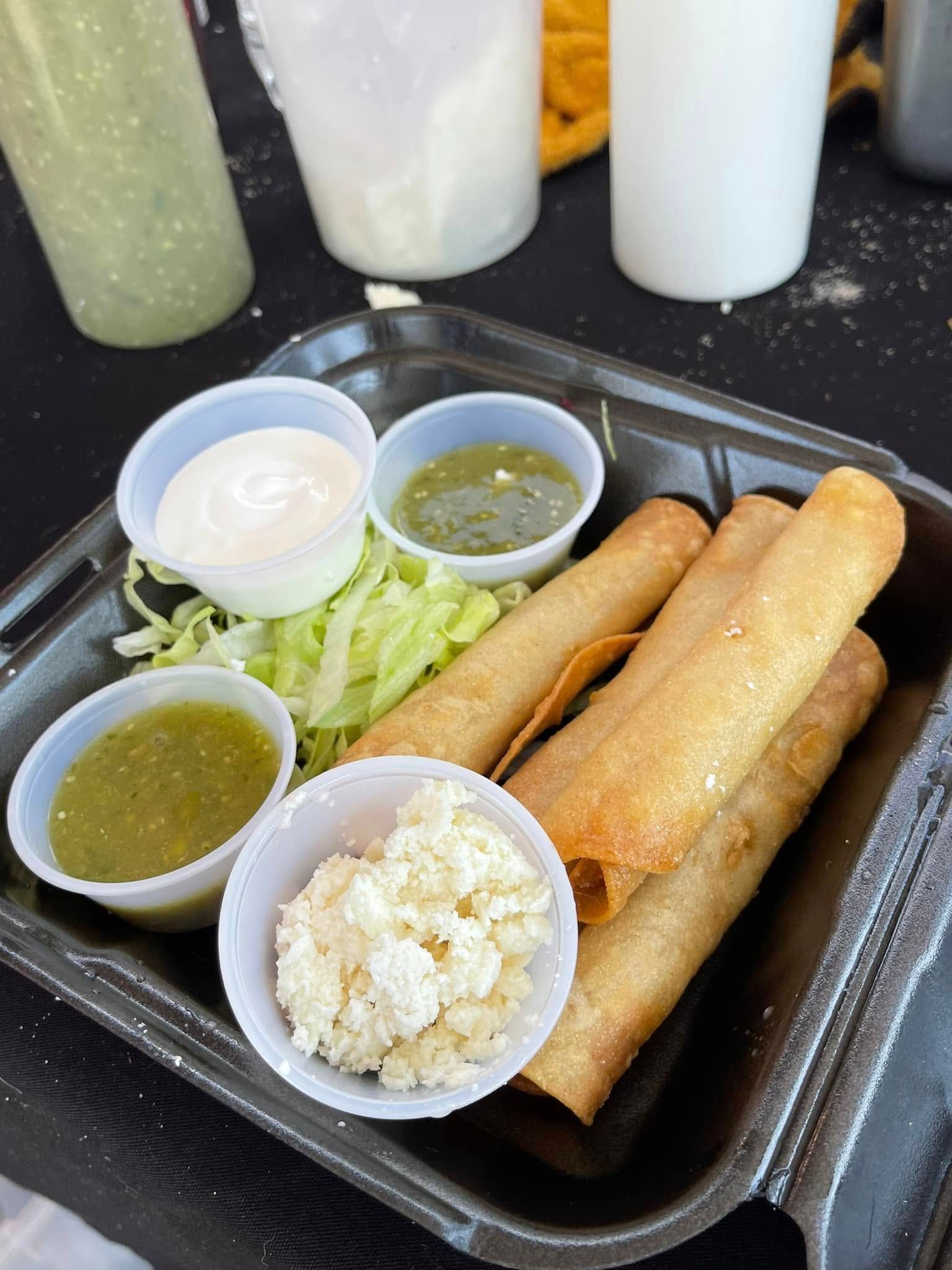 Tray of golden fried spring rolls with dipping sauces and shredded cabbage on a dark table.